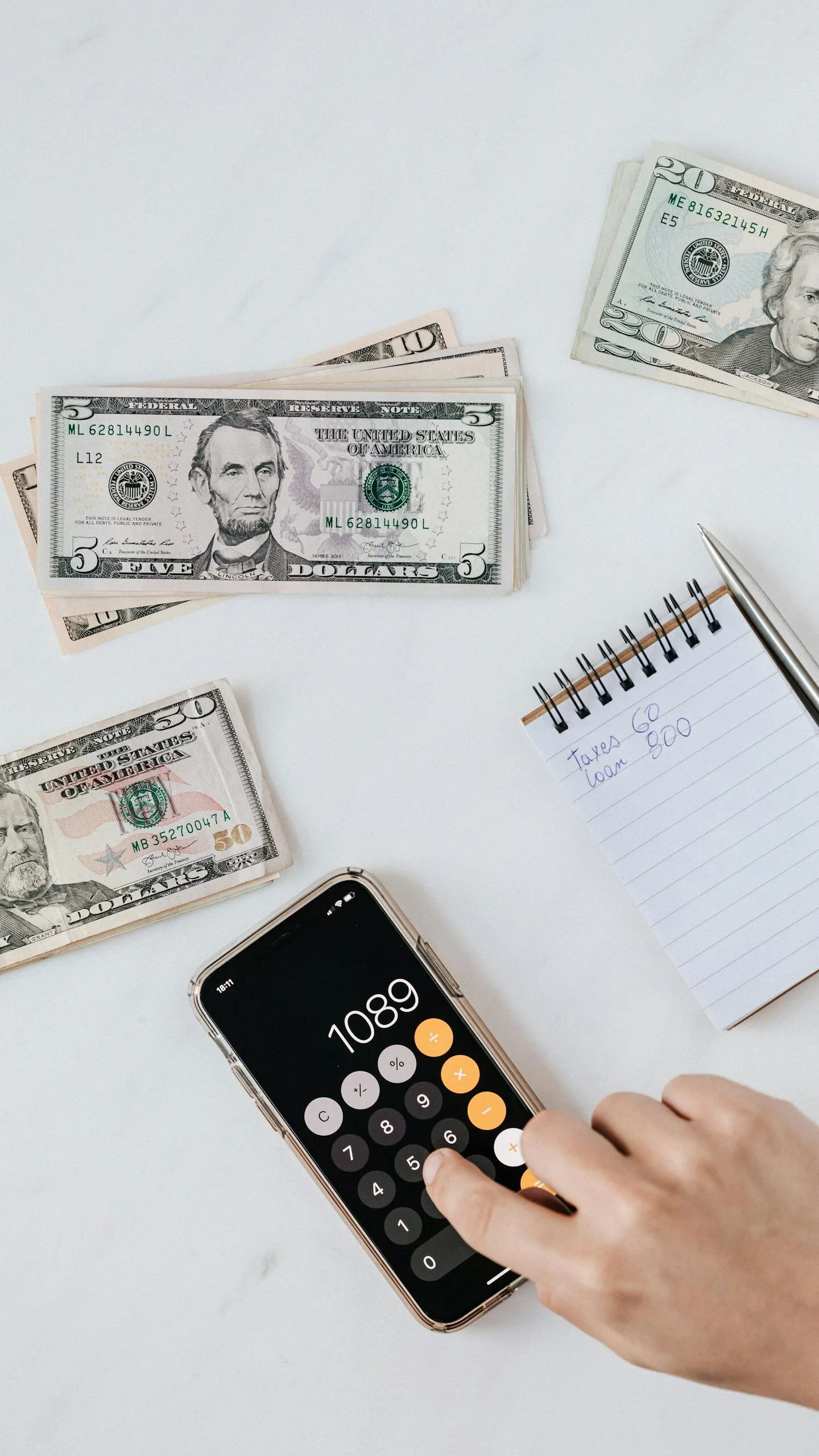 Overhead view of a hand using a calculator with US dollars and notes, representing finance and budgeting.