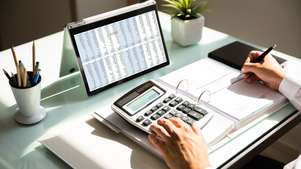 Pessoa organizando finanças pessoais em laptop com planilha de orçamento base zero.