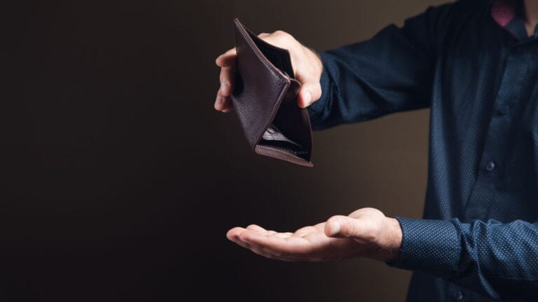 Pessoa segurando carteira vazia com expressão pensativa, representando preocupação com finanças.
