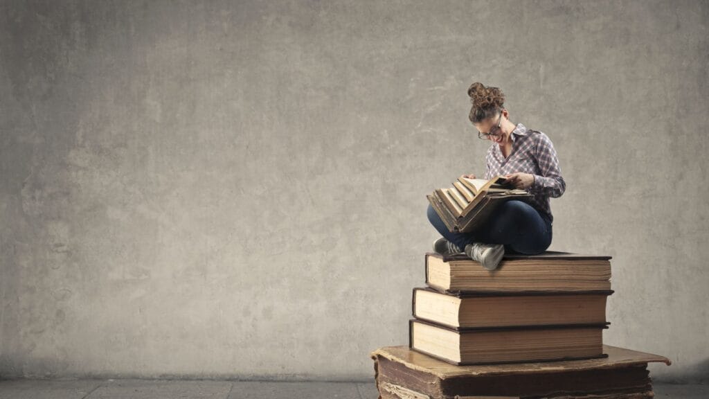 MULHER SENTADA SOBRE OS LIVROS REPRESENTANDO A SEÇAO DE LEITURA RECOMENDADA